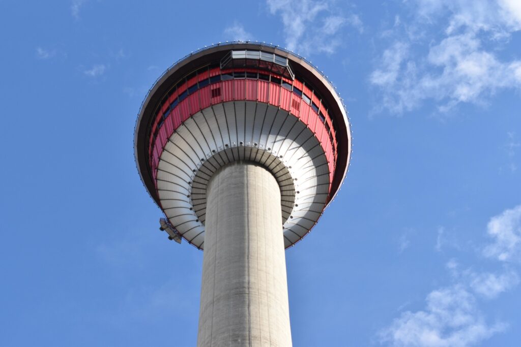 The Calgary Tower standing tall amidst downtown Calgary's skyline, viewed from street level against a clear blue sky