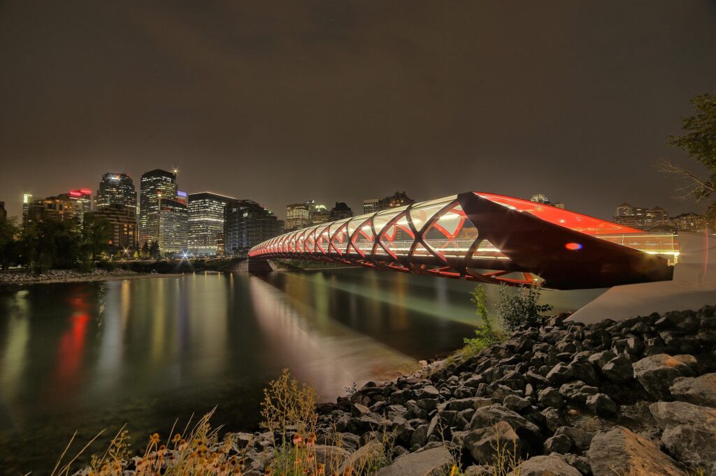 The iconic red Calgary Peace Bridge spanning the Bow River under a clear blue sky. Title: Calgary Peace Bridge